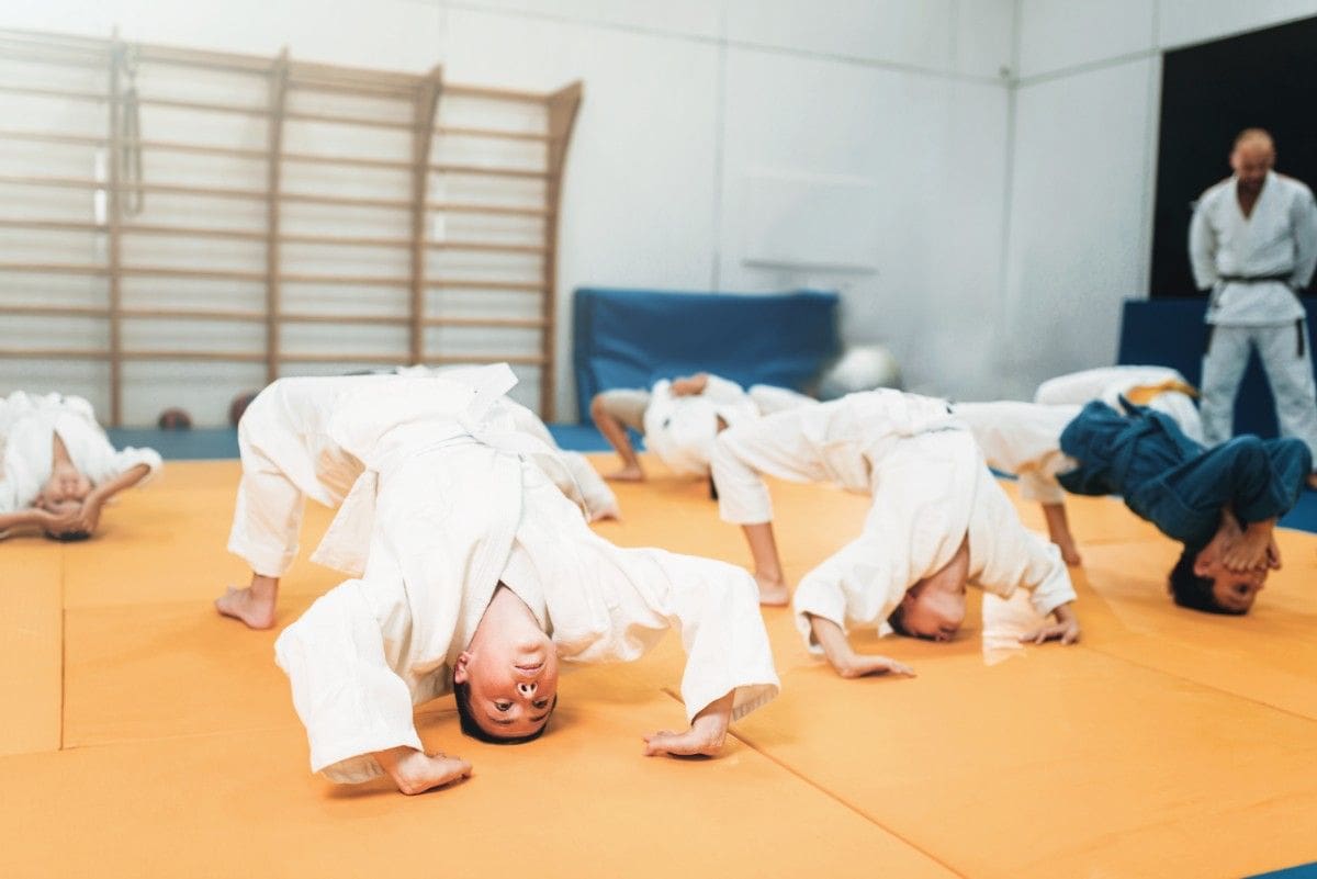 Preschool jiu jitsu class warming up with bridge exercises while instructor supervises